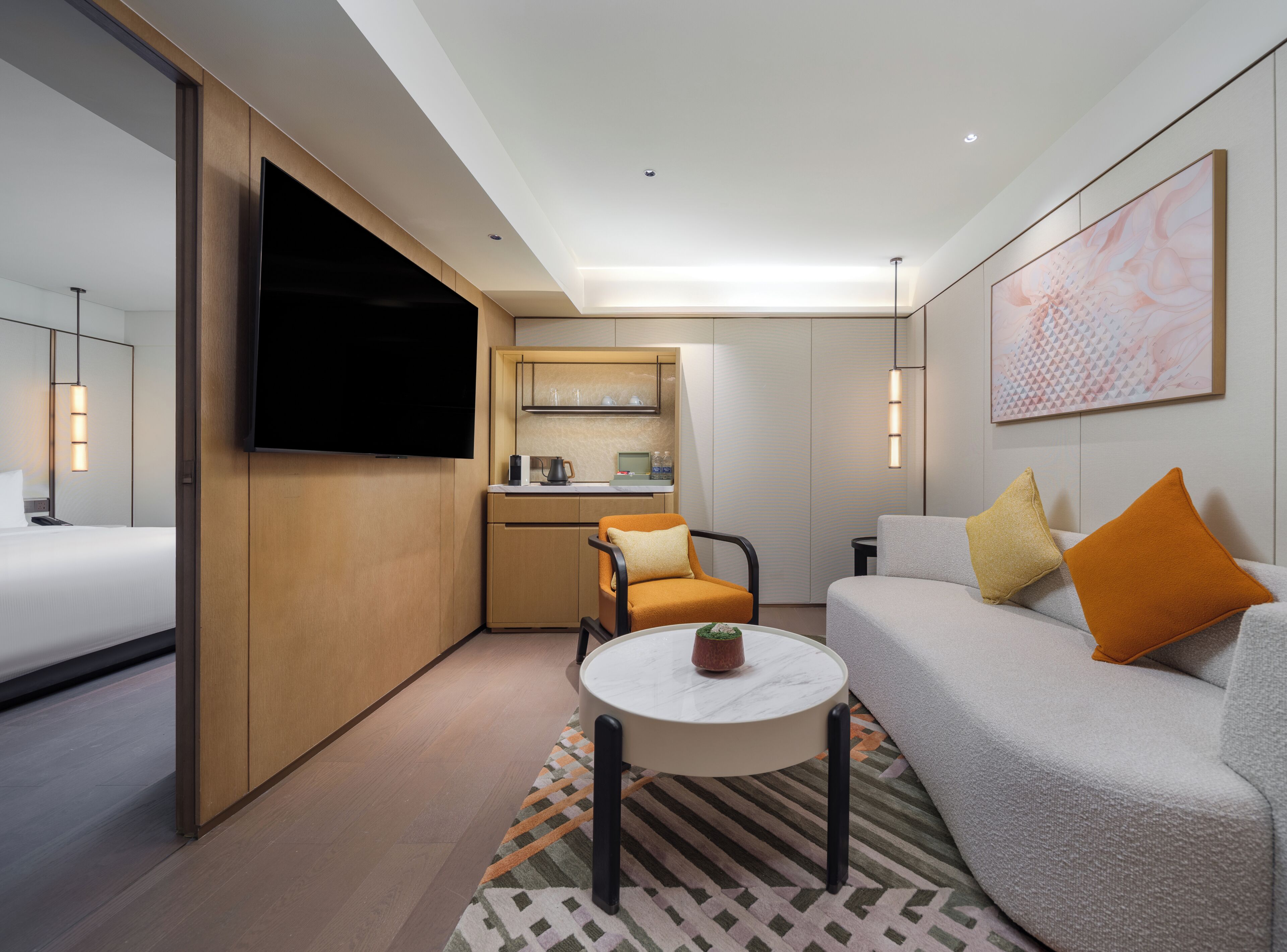 Habitación de hotel moderna con cama, sofá, una mesita, televisor, kitchenette y baño.
