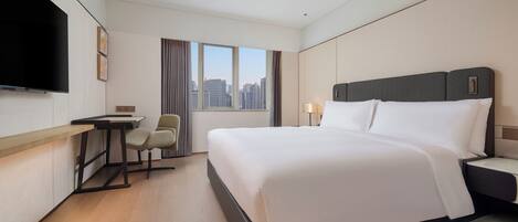 Quarto de hotel com cama, escrivaninha, cadeira, televisão e janela com vista para a cidade.