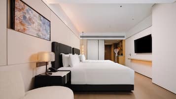 A modern hotel room with a large bed, bedside table, lamp, and a flat-screen TV mounted on the wall.