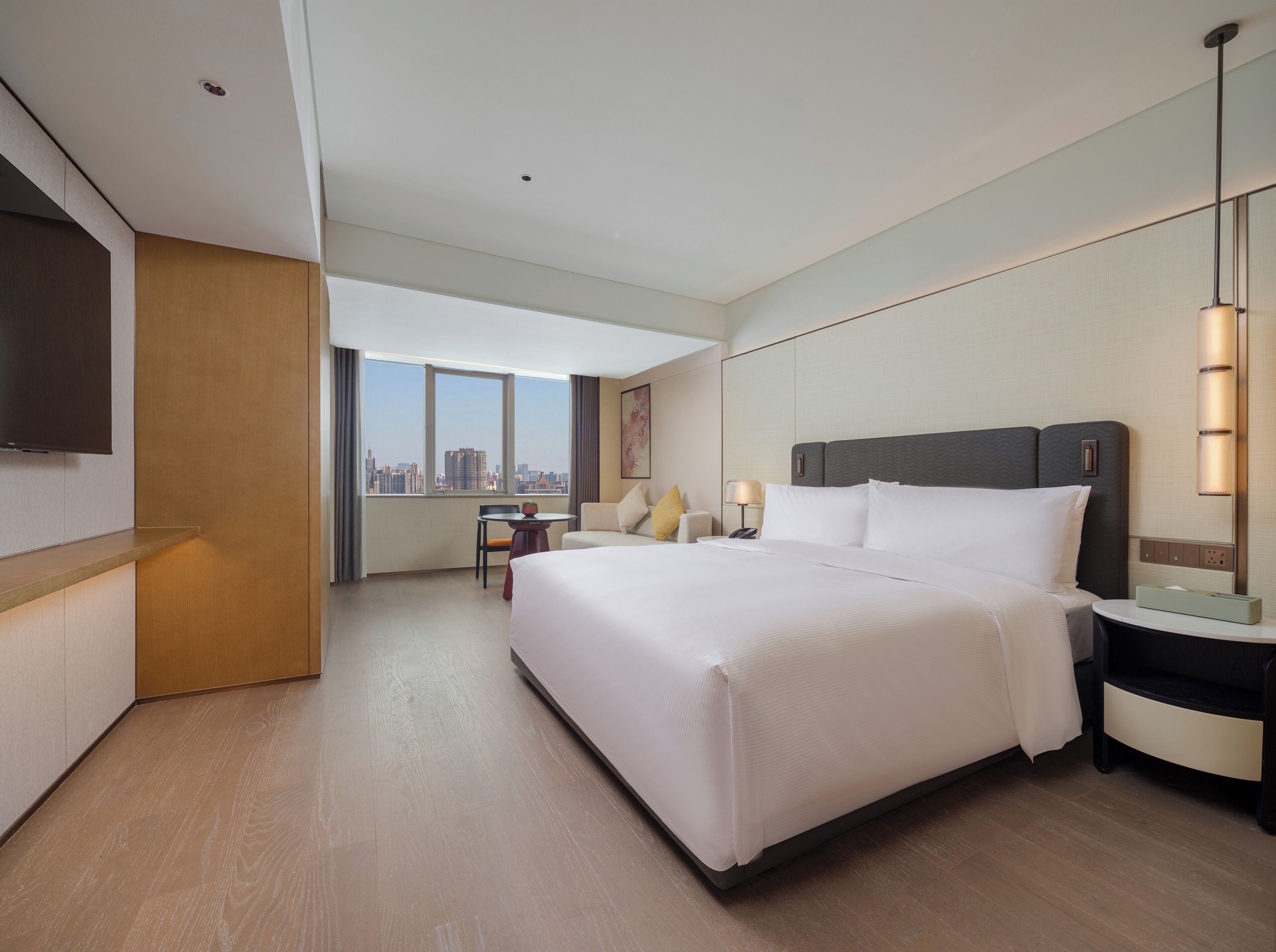 Une chambre d’hôtel avec un grand lit, un bureau, une chaise, une télévision et une vue sur la ville.