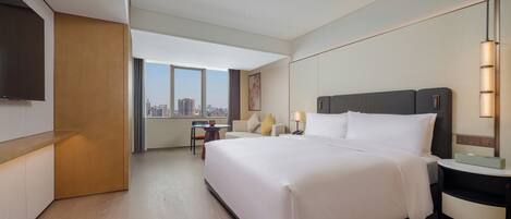 Habitación de hotel con una cama grande, un escritorio, una silla, un televisor y vistas a la ciudad.