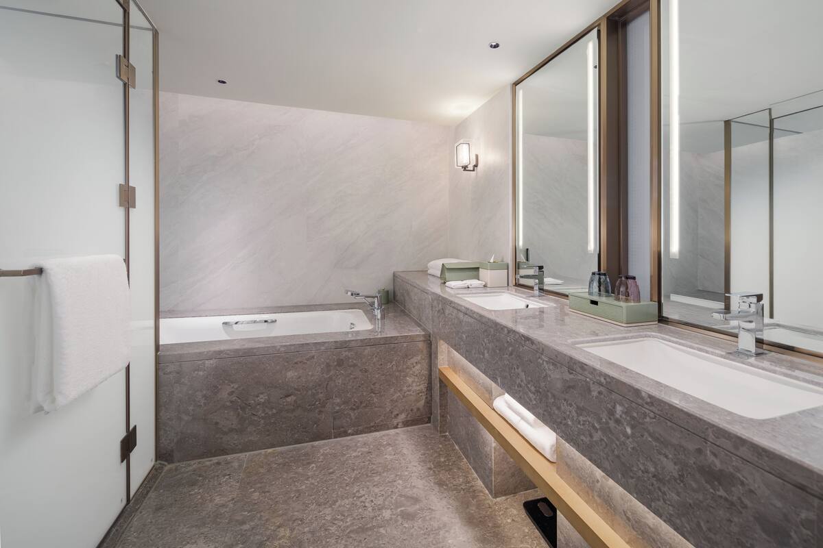 A modern bathroom with a large mirror, two sinks, a bathtub, and a towel rack.