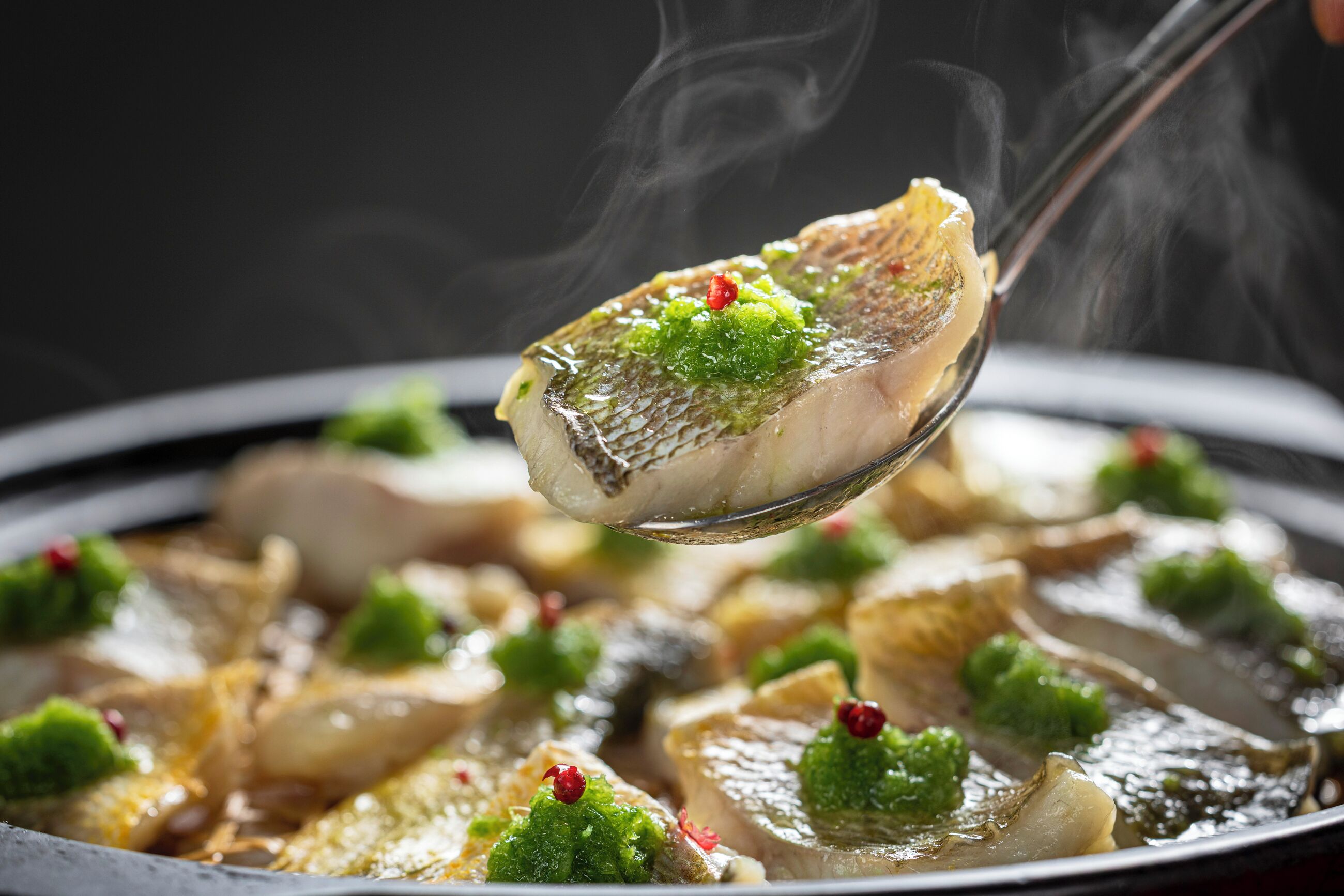 Un plato con pescado adornado con ingredientes verdes y rojos.