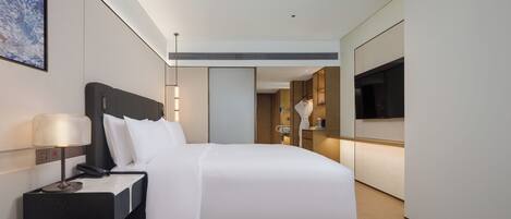 Una habitación de hotel moderna con una cama grande, mesita de noche, lámpara y televisor montado en la pared.