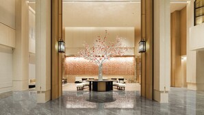 A lobby with a central tree sculpture, seating area, and a brick-patterned wall. - Canton Hotel Guangzhou, Tapestry Collection by Hilton (Guangzhou)