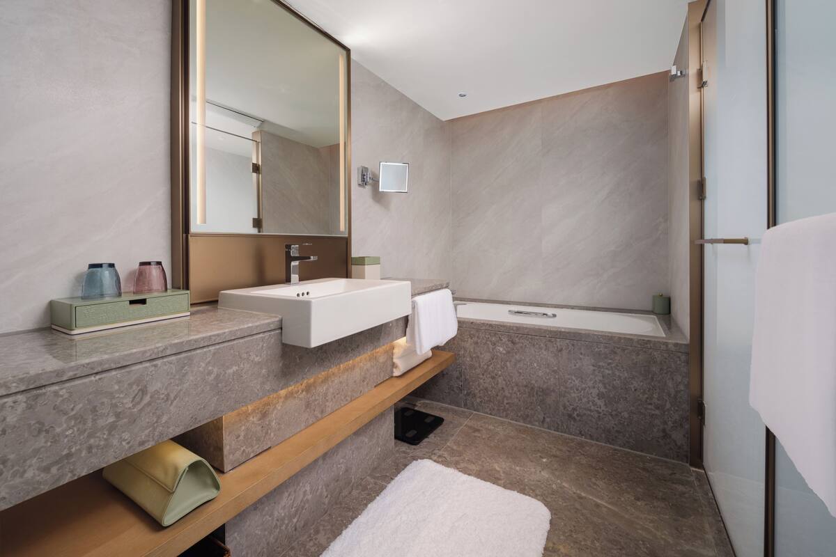 A modern bathroom with a large mirror, a sink, and a bathtub.