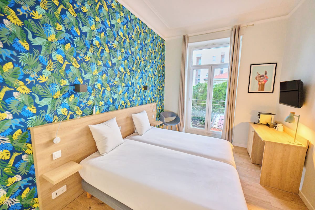 A hotel room with a bed, a desk, a chair, a TV, and a window with a view.