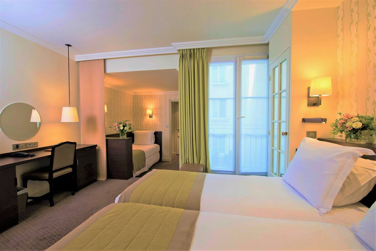 A hotel room with a bed, a desk, a chair, a mirror, and a bathroom visible through an open door.