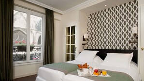 A hotel room with a large bed, a window with curtains, a patterned wall, and a breakfast tray on the bed. - Hôtel Henri IV Rive Gauche (Paris)