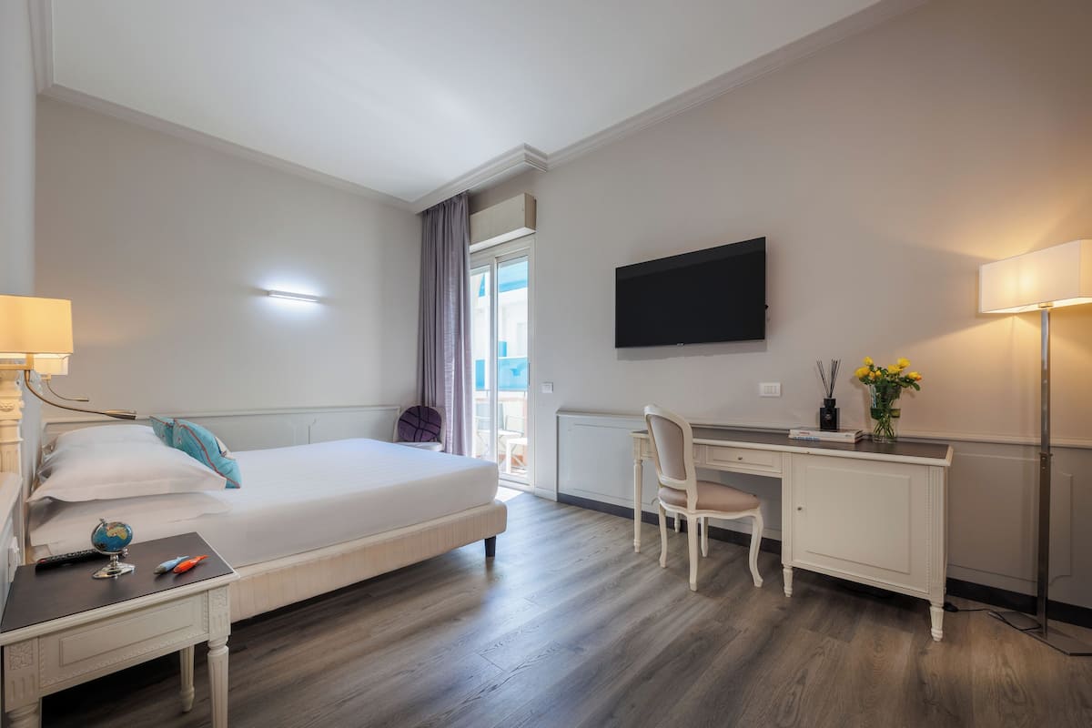 A hotel room with a bed, desk, chair, and a TV on the wall.