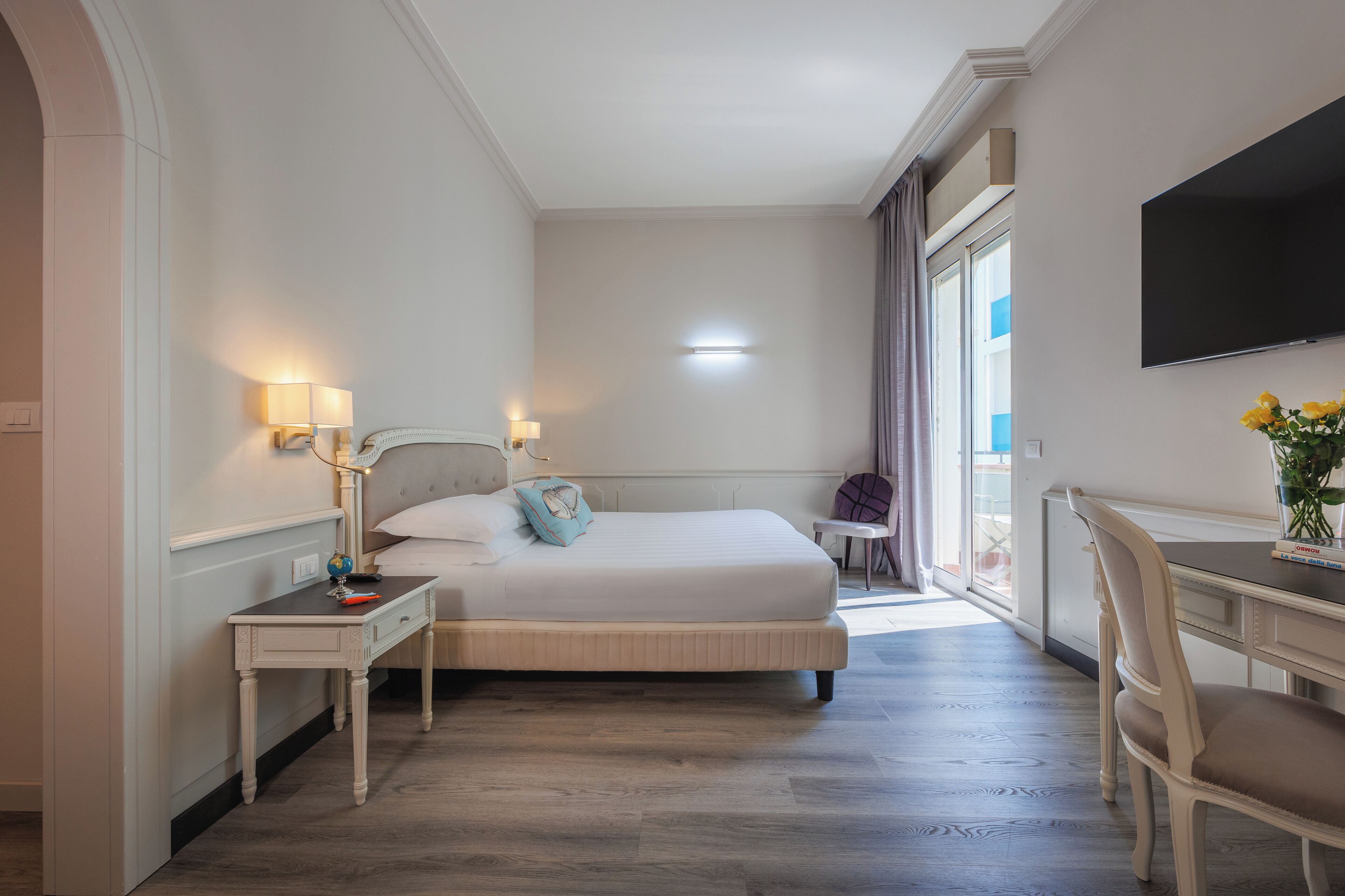 A hotel room with a bed, bedside table, lamp, TV, and a desk with a chair.