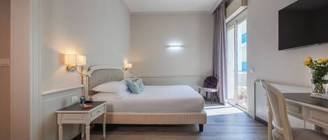 A hotel room with a bed, bedside table, lamp, TV, and a desk with a chair.