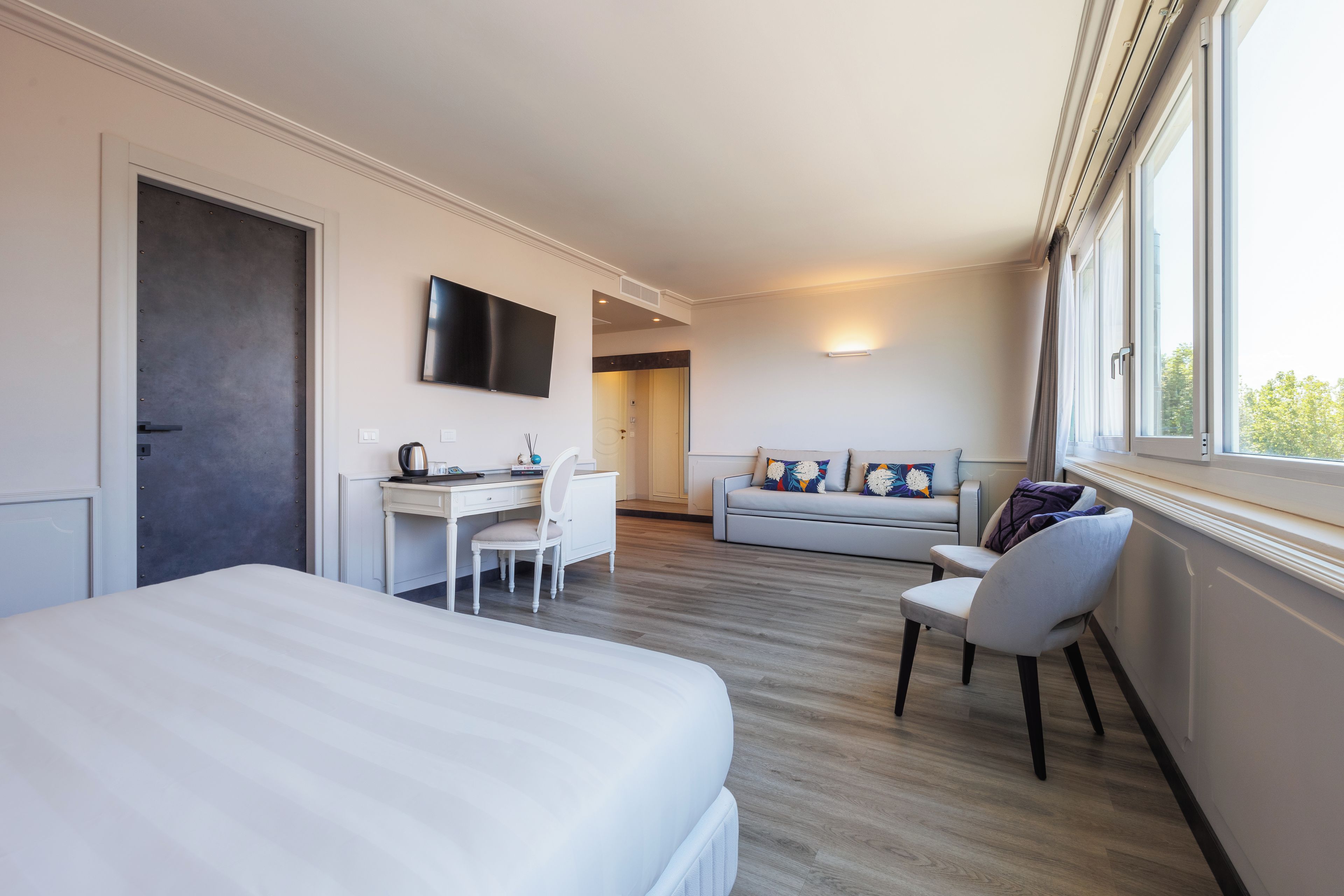 A hotel room with a bed, a desk with a chair, a sofa, and a TV mounted on the wall.
