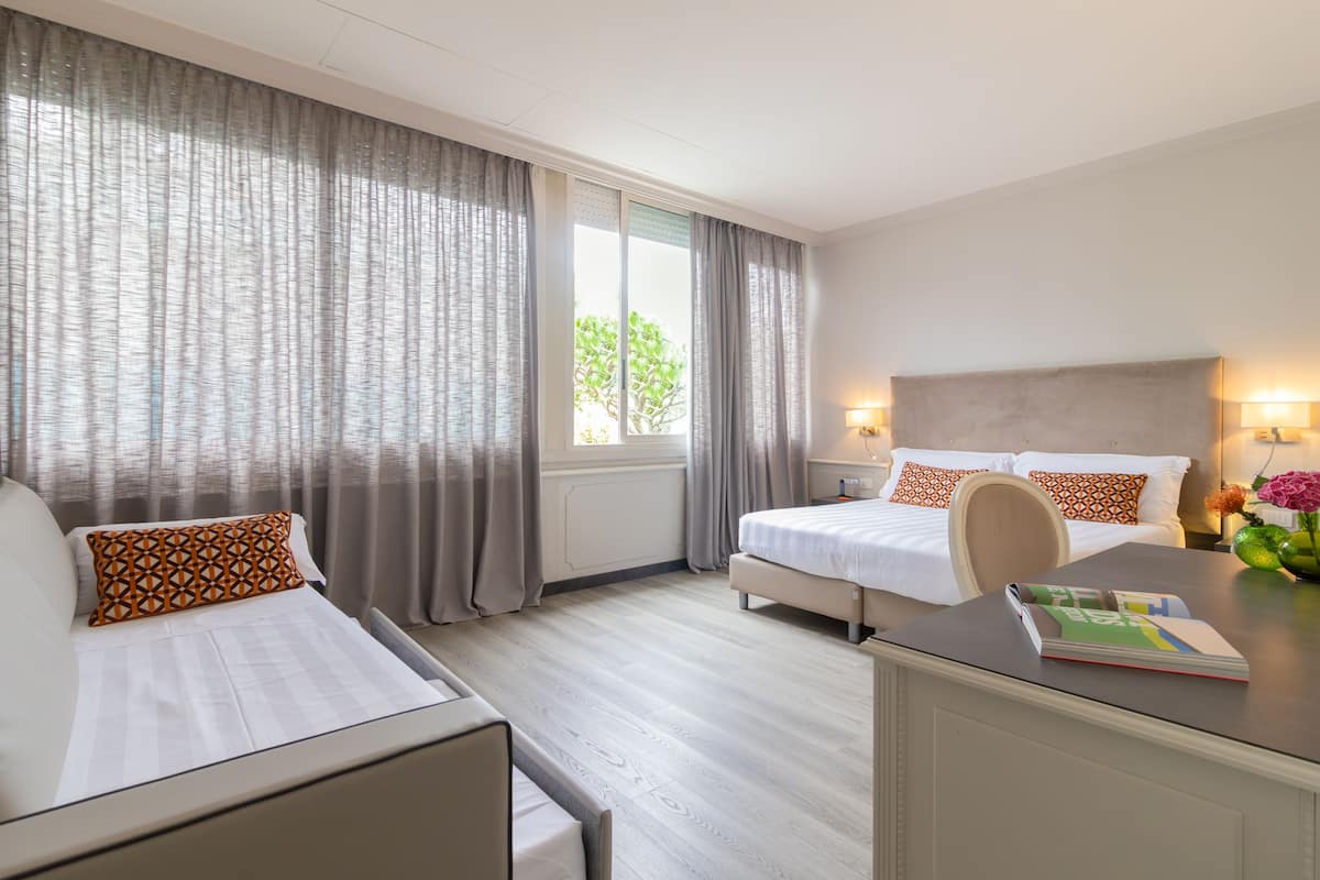 A hotel room with two beds, a desk, and a window with curtains.