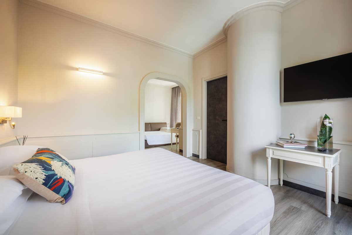 A hotel room with a large bed, a desk, a television, and a mirror.