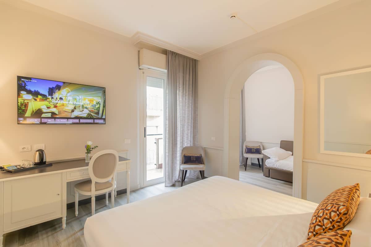 A hotel room with a bed, a desk, a chair, a TV, and a balcony with a view.