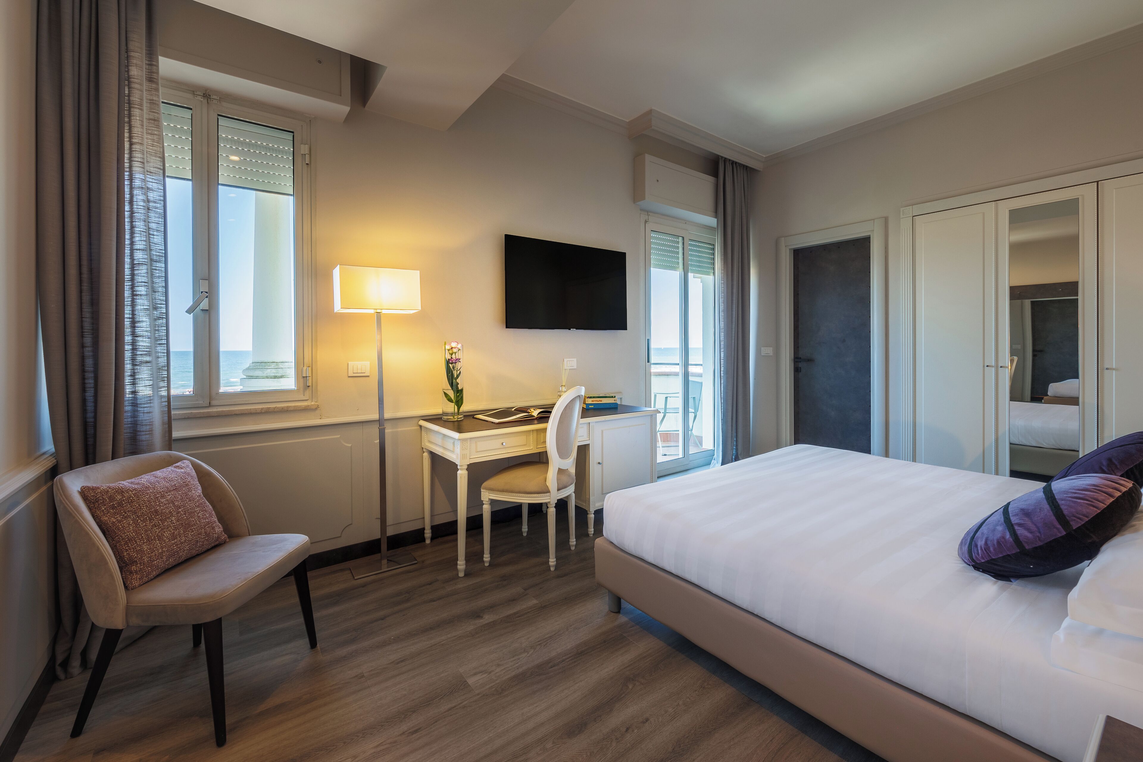 A hotel room with a bed, a desk, a chair, a TV, and a window with curtains.