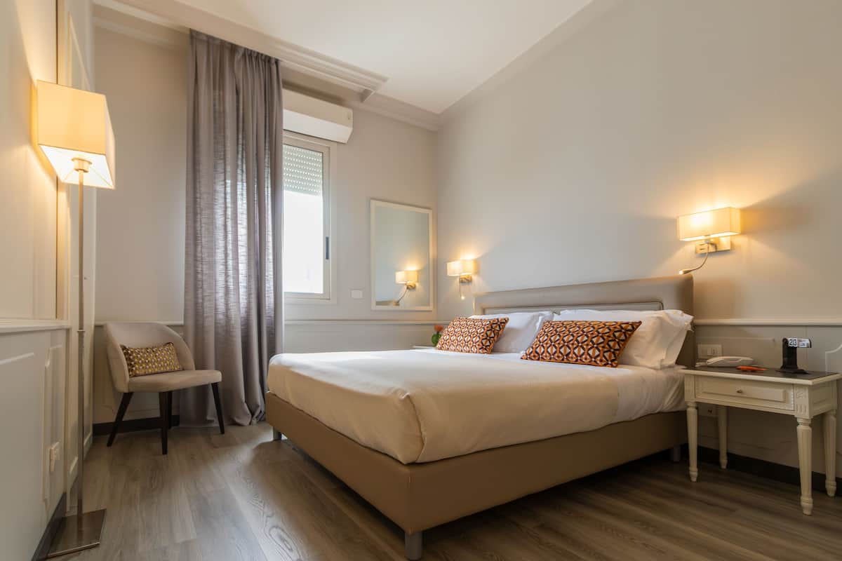 A hotel room with a large bed, bedside lamps, a chair, and a nightstand.