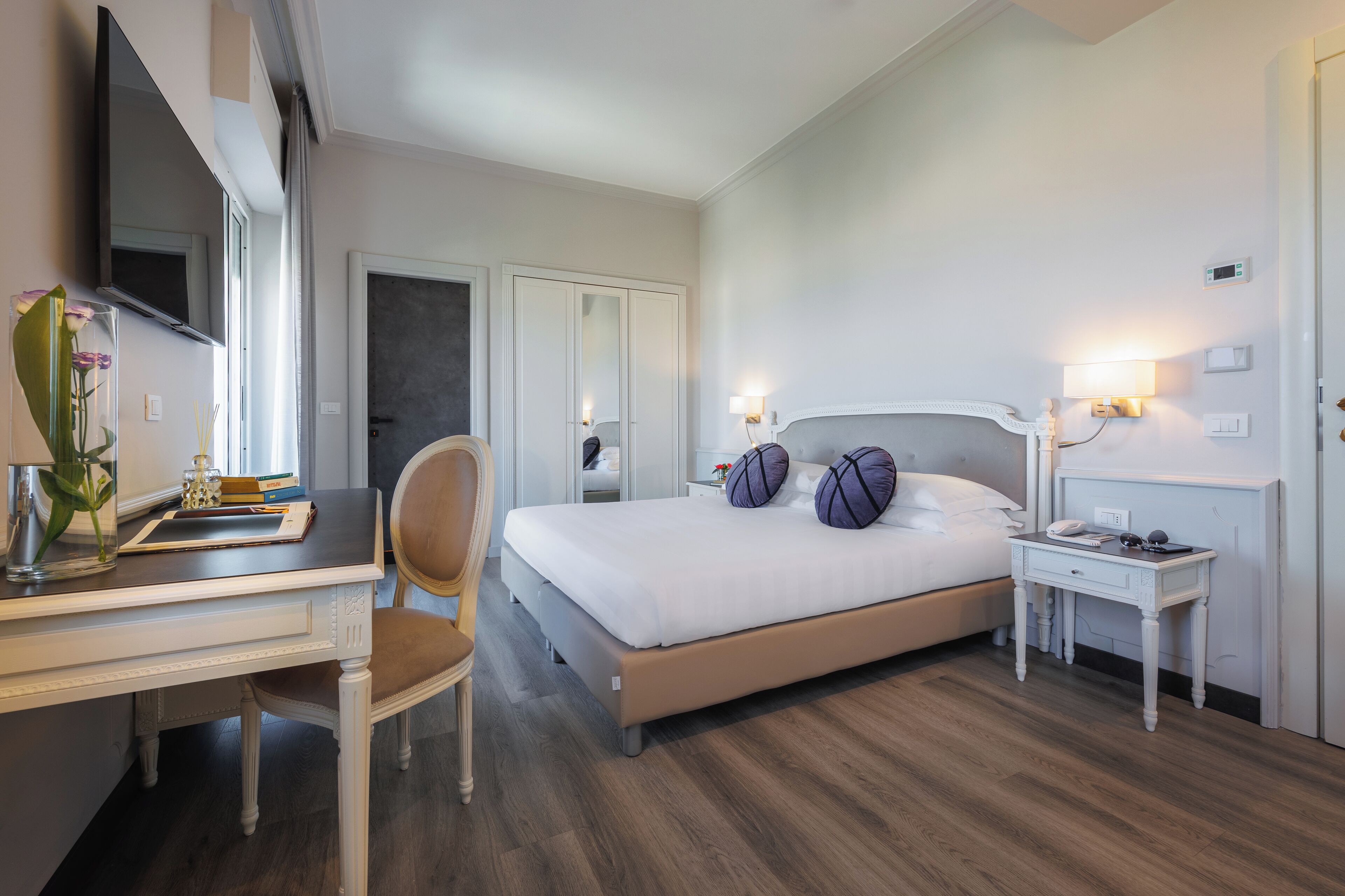 A hotel room with a bed, a desk, a chair, a TV, and a bedside table.