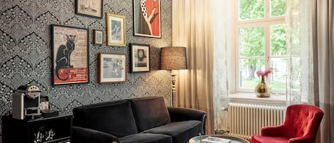 A living room with a black sofa, a red armchair, a coffee table, and a window with curtains.