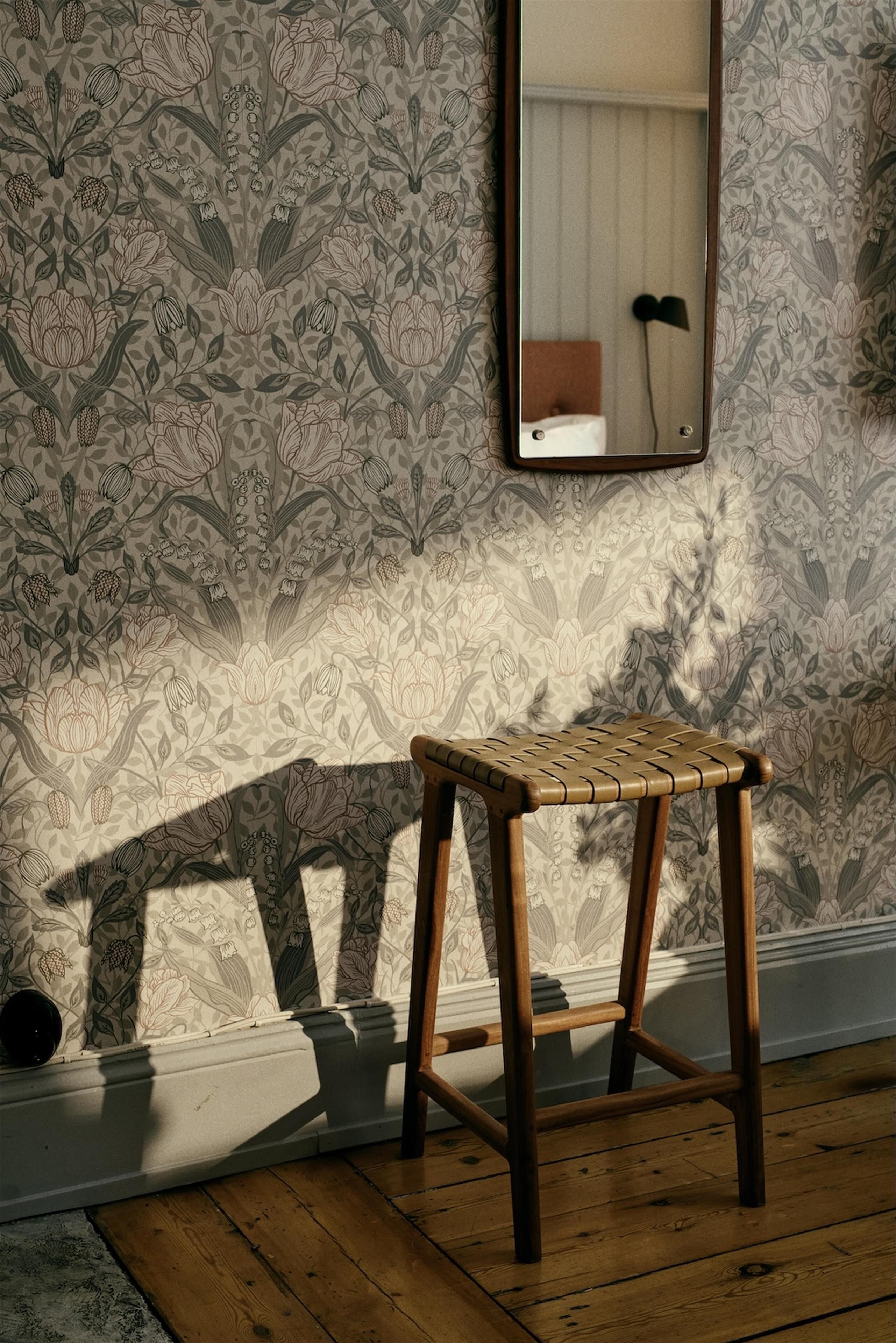 A wooden stool in a room with patterned wallpaper and a mirror on the wall.
