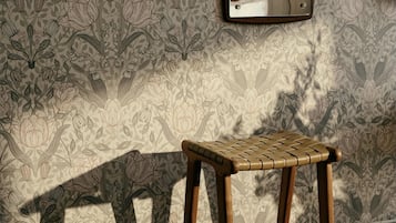 A wooden stool in a room with patterned wallpaper and a mirror on the wall.