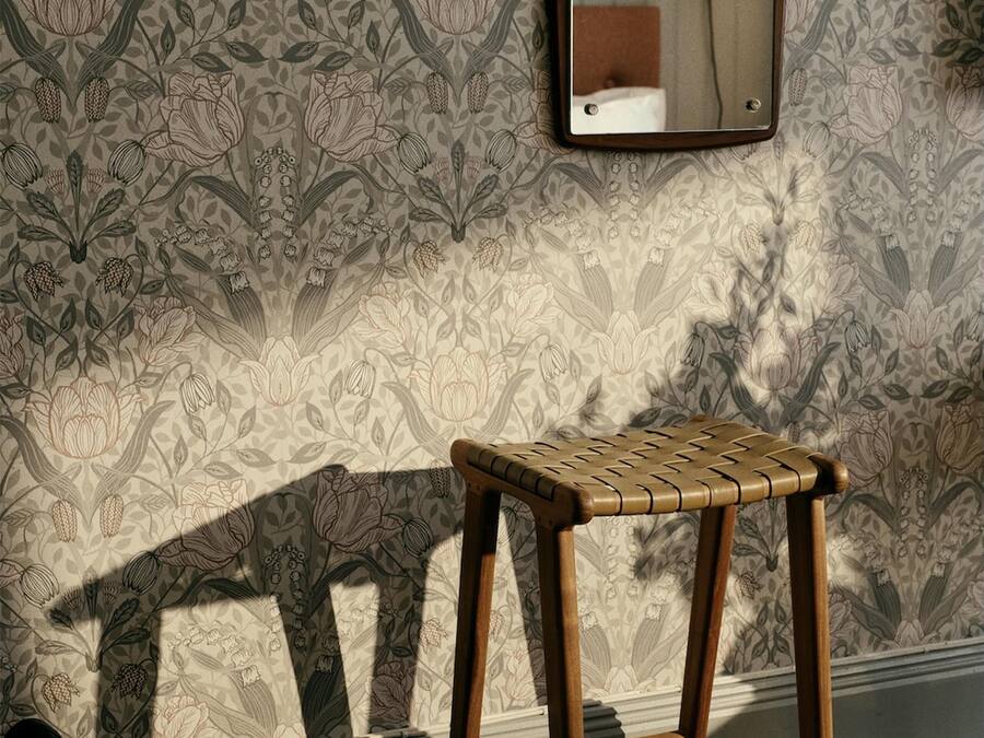 A wooden stool in a room with patterned wallpaper and a mirror on the wall.