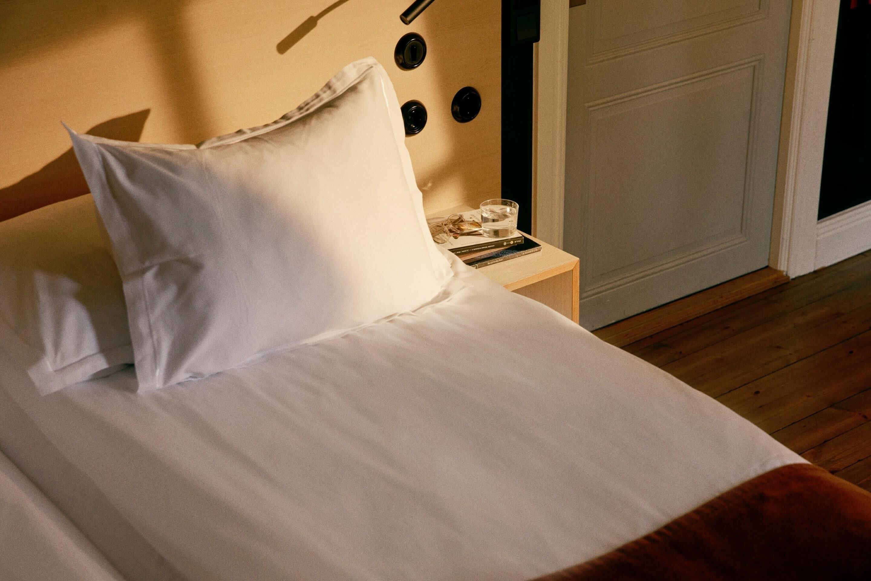 A neatly made bed with white linens and pillows, a bedside table with a glass of water, and a book.