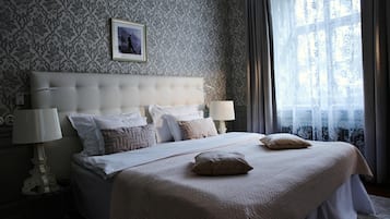 Ein Schlafzimmer mit einem gesteppten Kopfteil, einem großen Bett mit vielen Kissen, einem Nachttisch mit einer Lampe und einem Fenster mit Vorhängen.