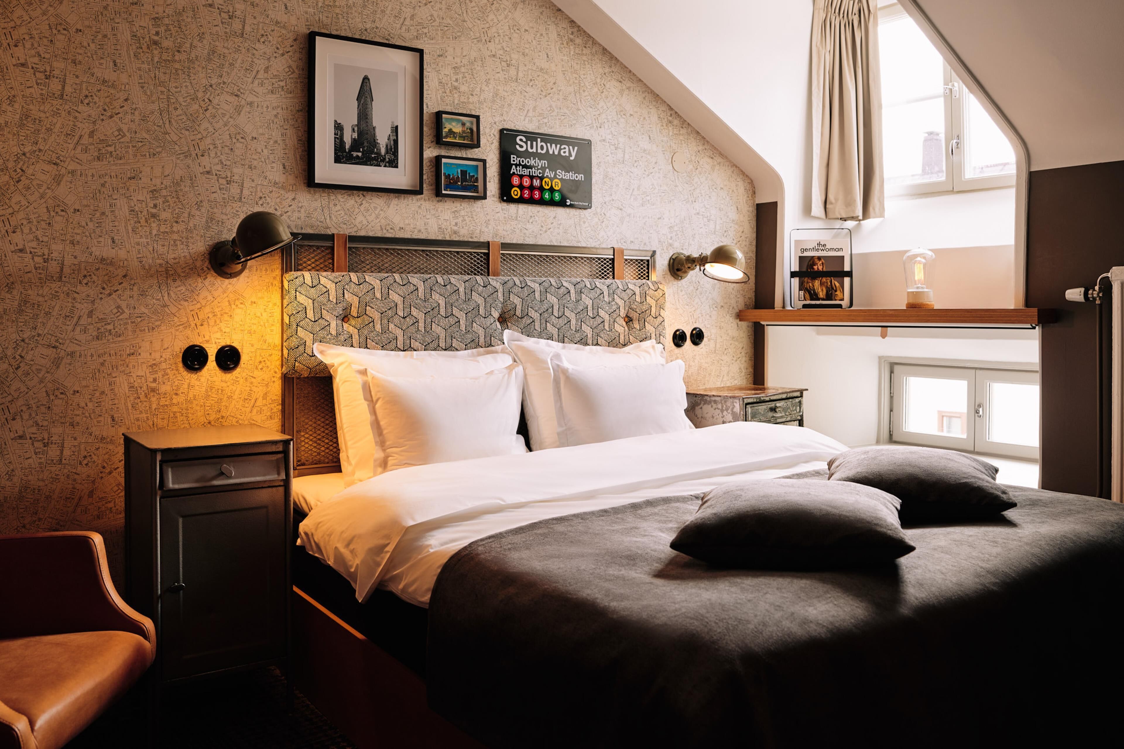 A hotel room with a bed, a nightstand, a lamp, a framed map, and a Subway sign.