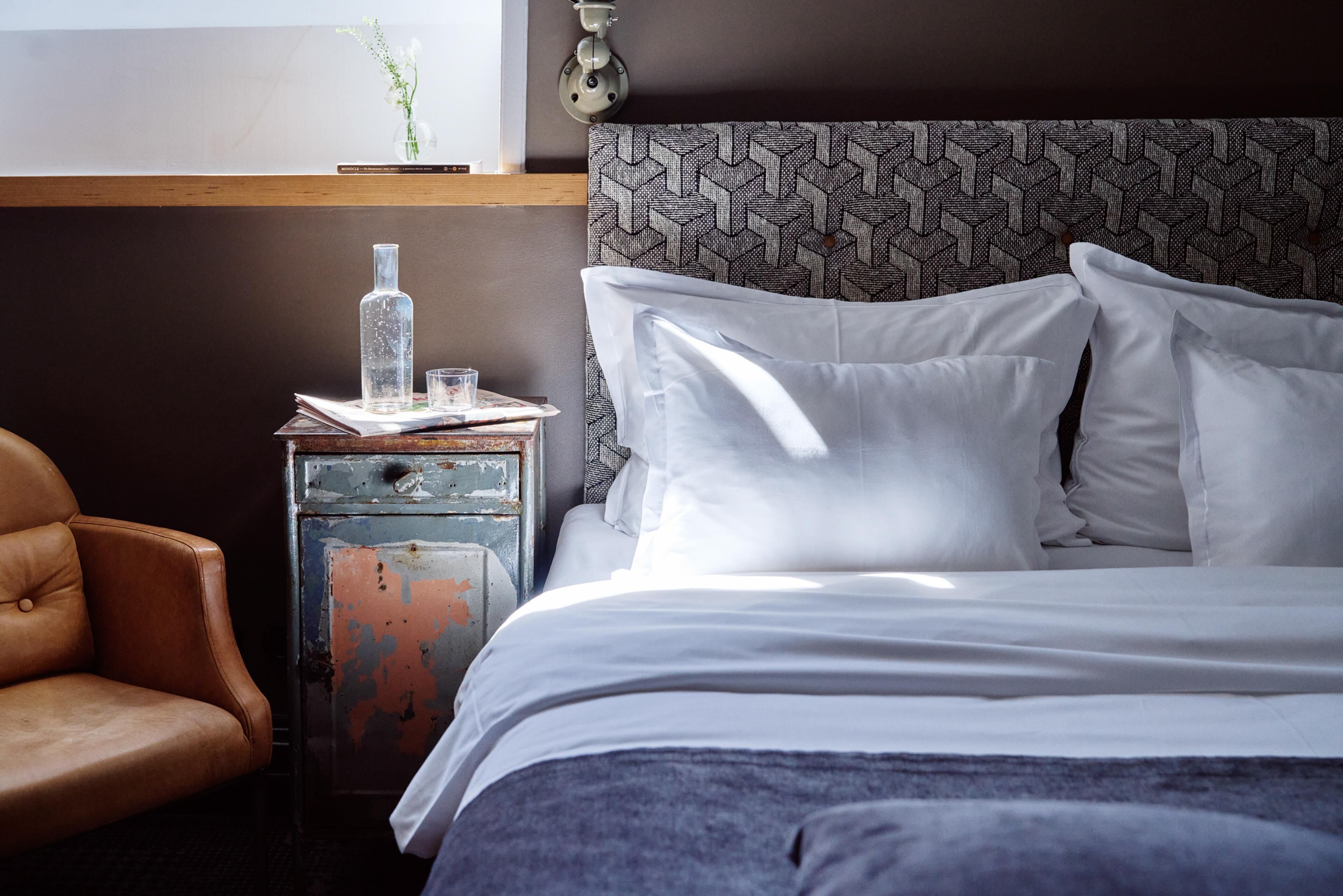A bedroom with a bed, a nightstand, a chair, and a wall-mounted lamp.