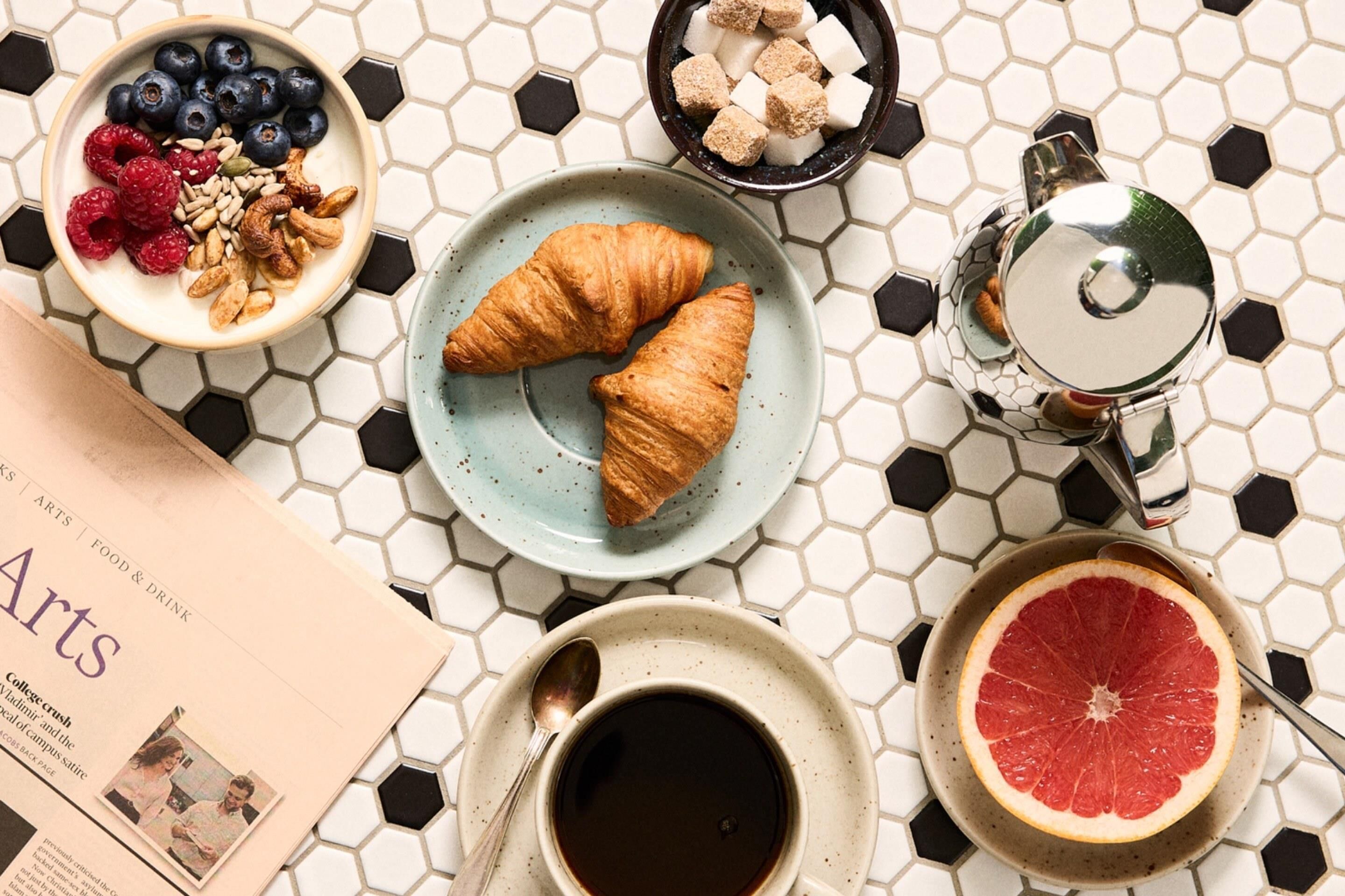 Desayuno con croissants, pomelo, café y un periódico.
