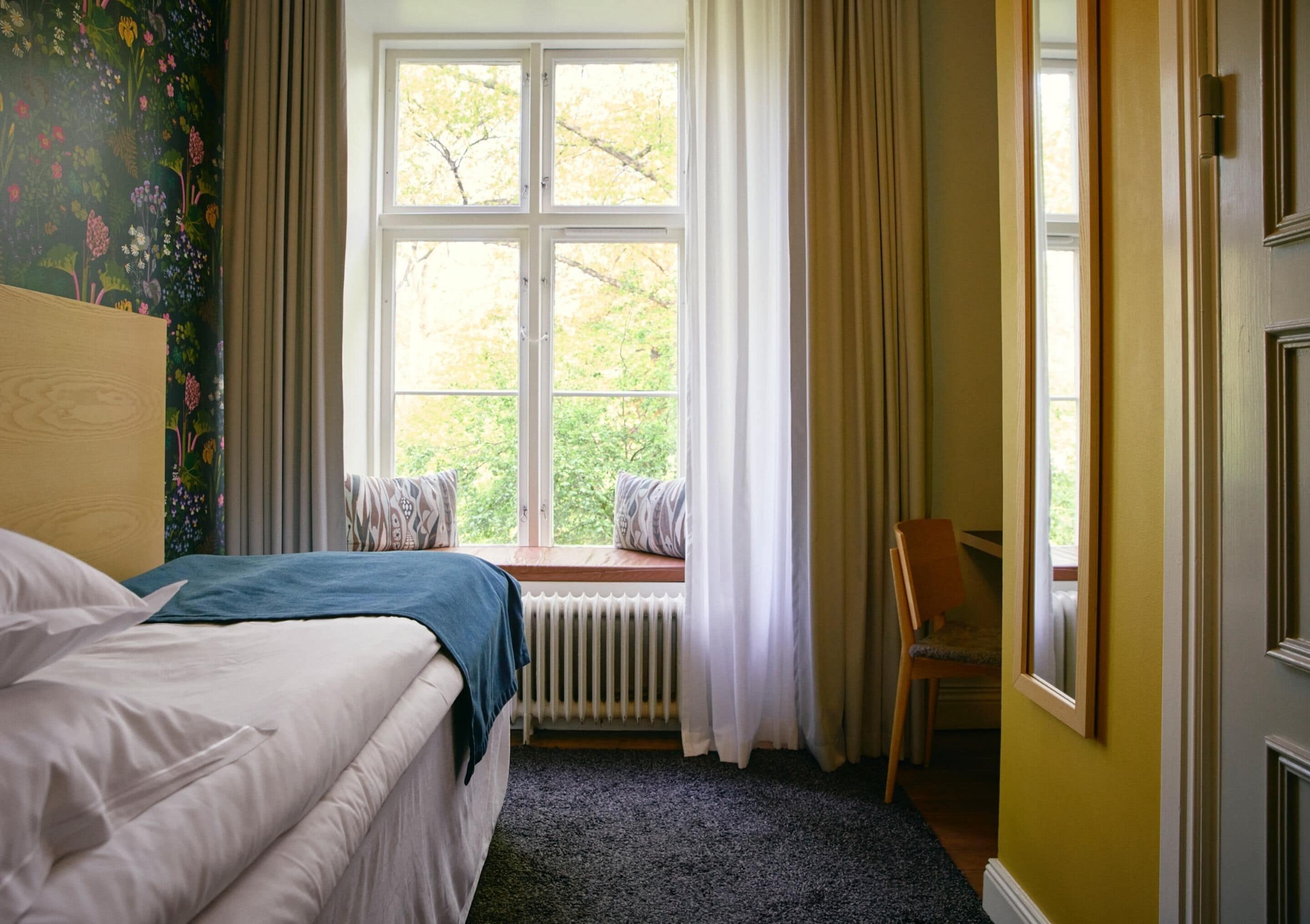Ein Schlafzimmer mit einem Bett, einem Fenster mit Vorhängen, einer Heizung und einem Sessel.