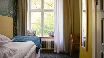 Ein Schlafzimmer mit einem Bett, einem Fenster mit Vorhängen, einer Heizung und einem Sessel.