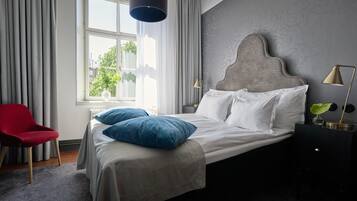 Ein Schlafzimmer mit einem Bett, einem roten Sessel, einem Fenster mit Vorhängen und einer Lampe.