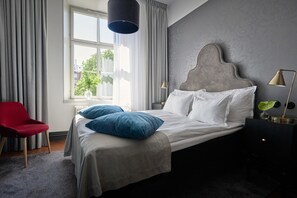 Un dormitorio con cama, una silla roja, una ventana con cortinas y una lámpara.