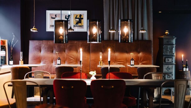 Interior de restaurante con cabinas de cuero, lámparas colgantes y una estufa antigua.