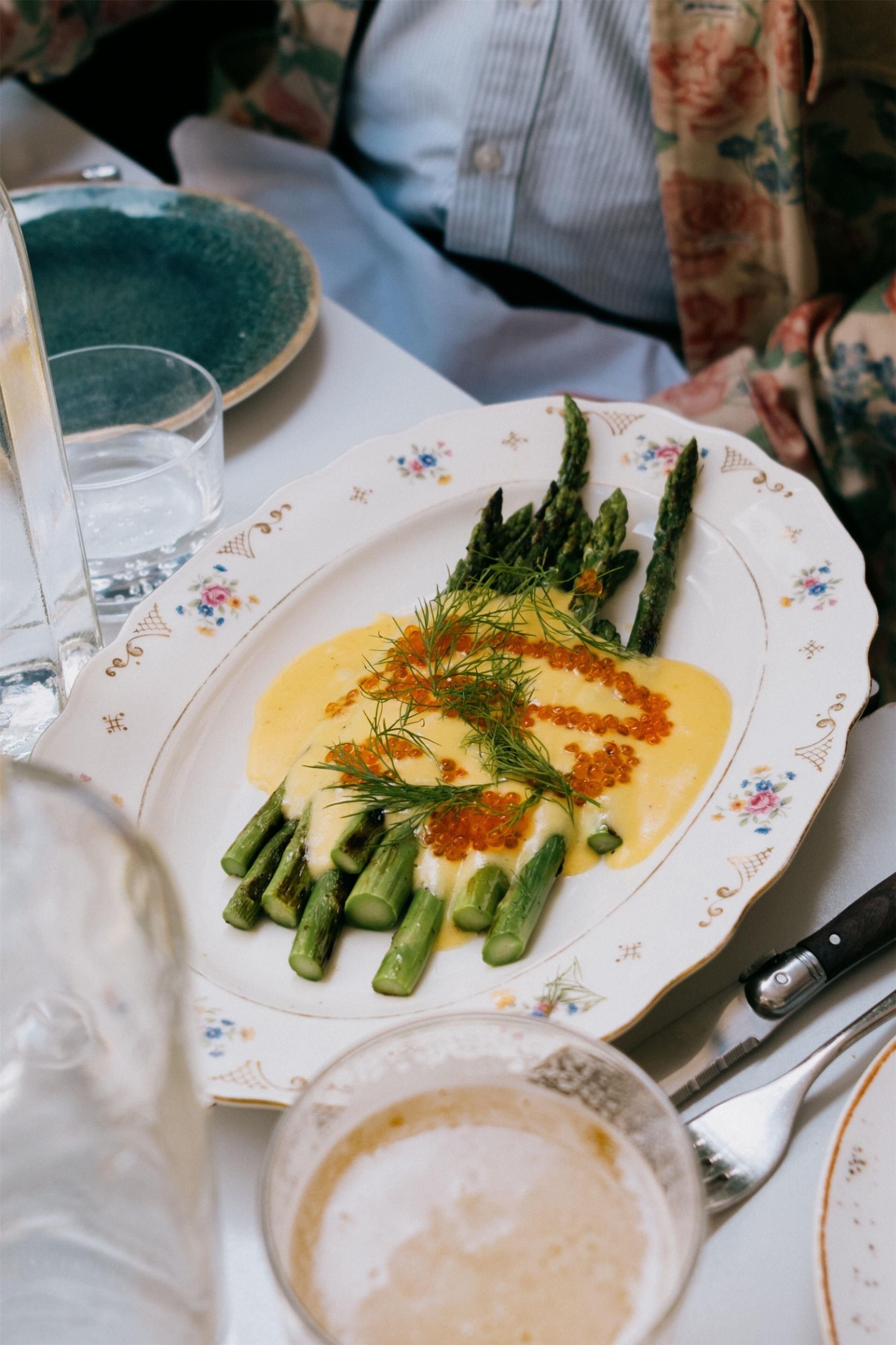 A plate of food with asparagus and a creamy sauce, accompanied by a knife and a glass.