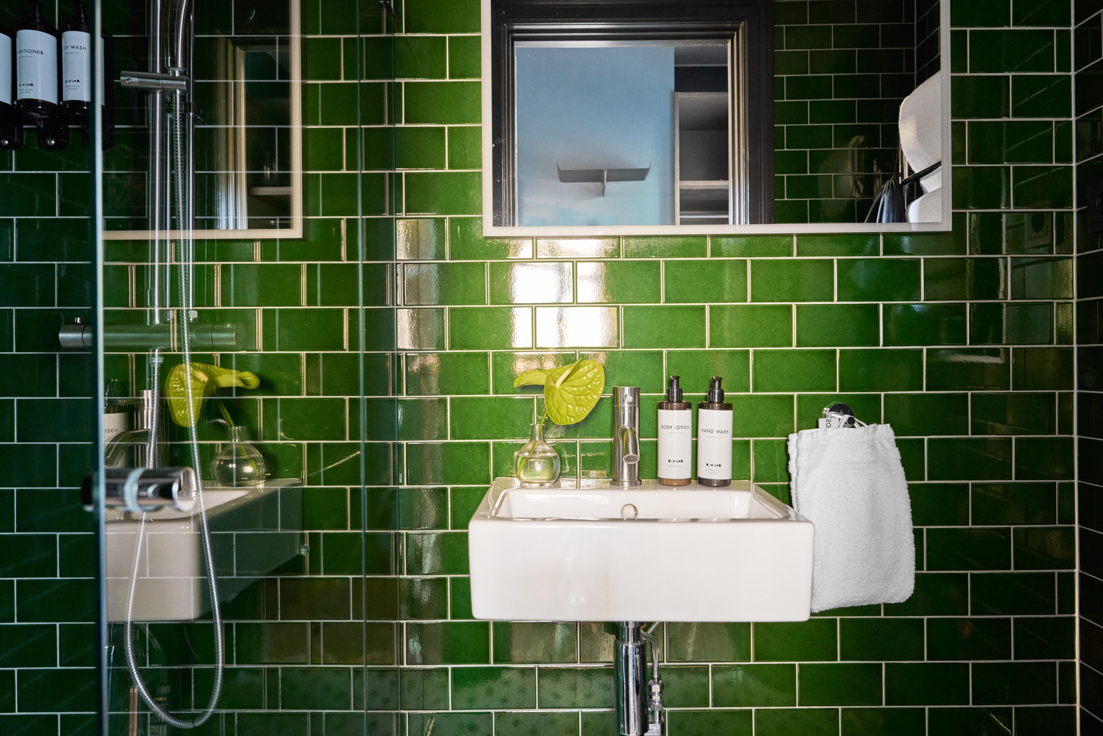 A bathroom with green tiles, a white sink, and toiletries.