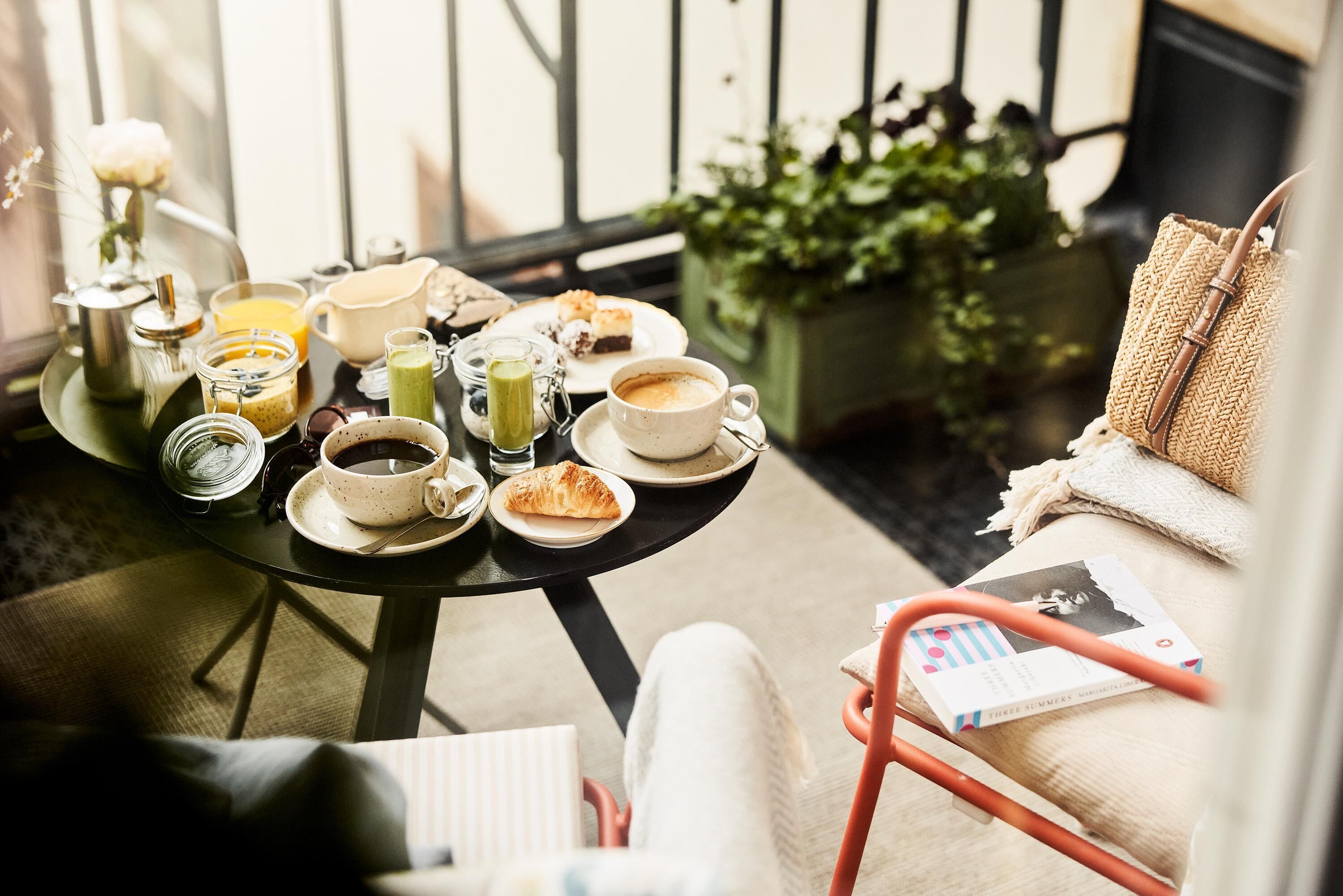 Desayuno listo en un balcón, con una mesa, sillas y una variedad de alimentos y bebidas.
