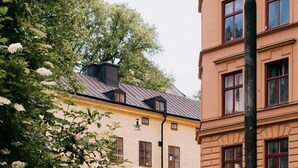 A street view with a yellow building, a black fence, and a tree with white flowers. - NOFO Hotel, WorldHotels Crafted (Stockholm)