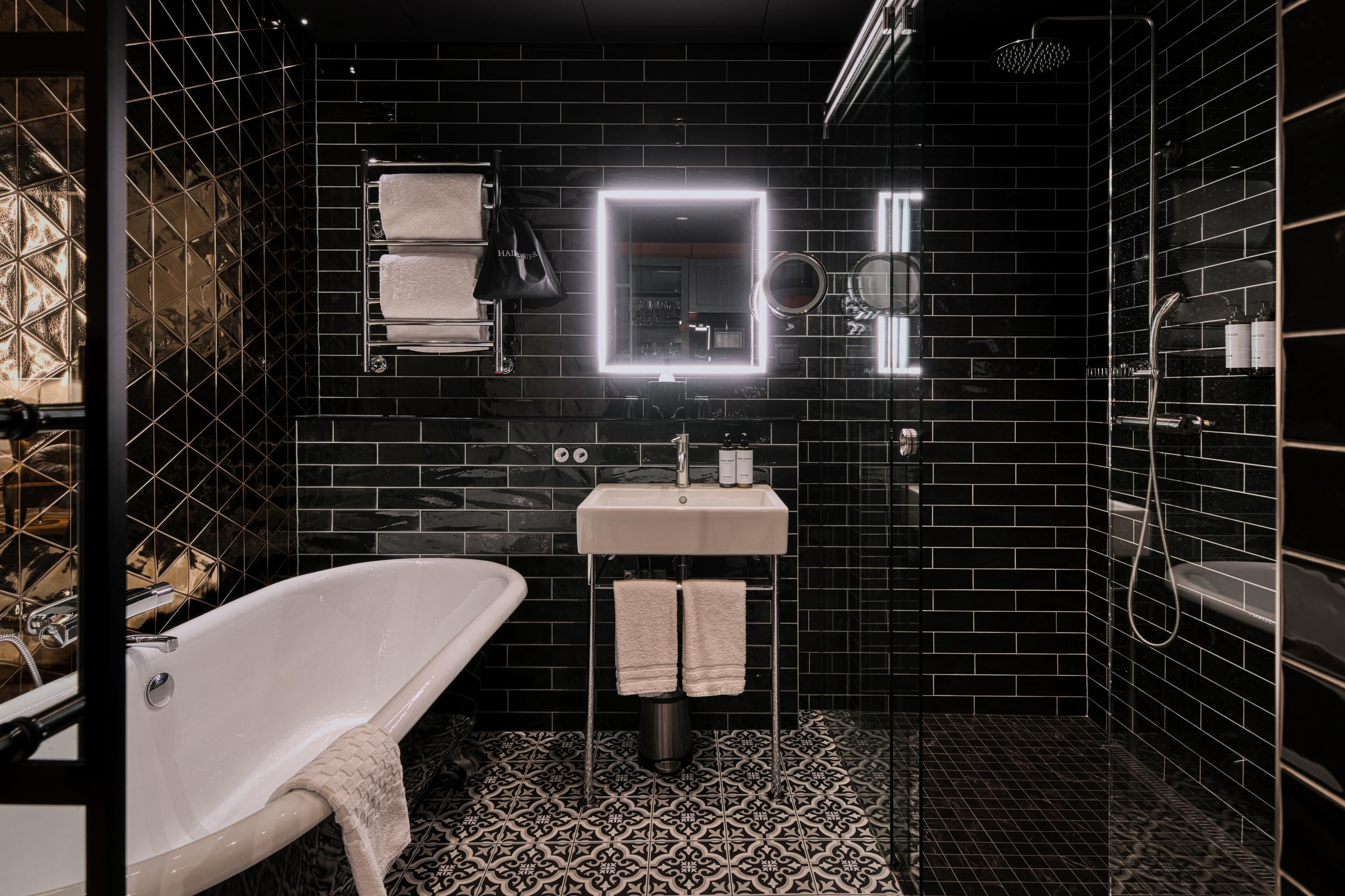 Ein modernes Badezimmer mit freistehender Badewanne, einem Waschtisch mit Spiegel und schwarzen Fliesenwänden.
