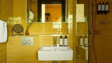 Baño con pared de azulejos amarillos, un lavamanos blanco, un espejo y artículos de tocador en la pared.
