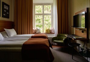A hotel room with a bed, a desk with a chair, a television, and a window with a view of trees. - NOFO Hotel, WorldHotels Crafted (Stockholm)
