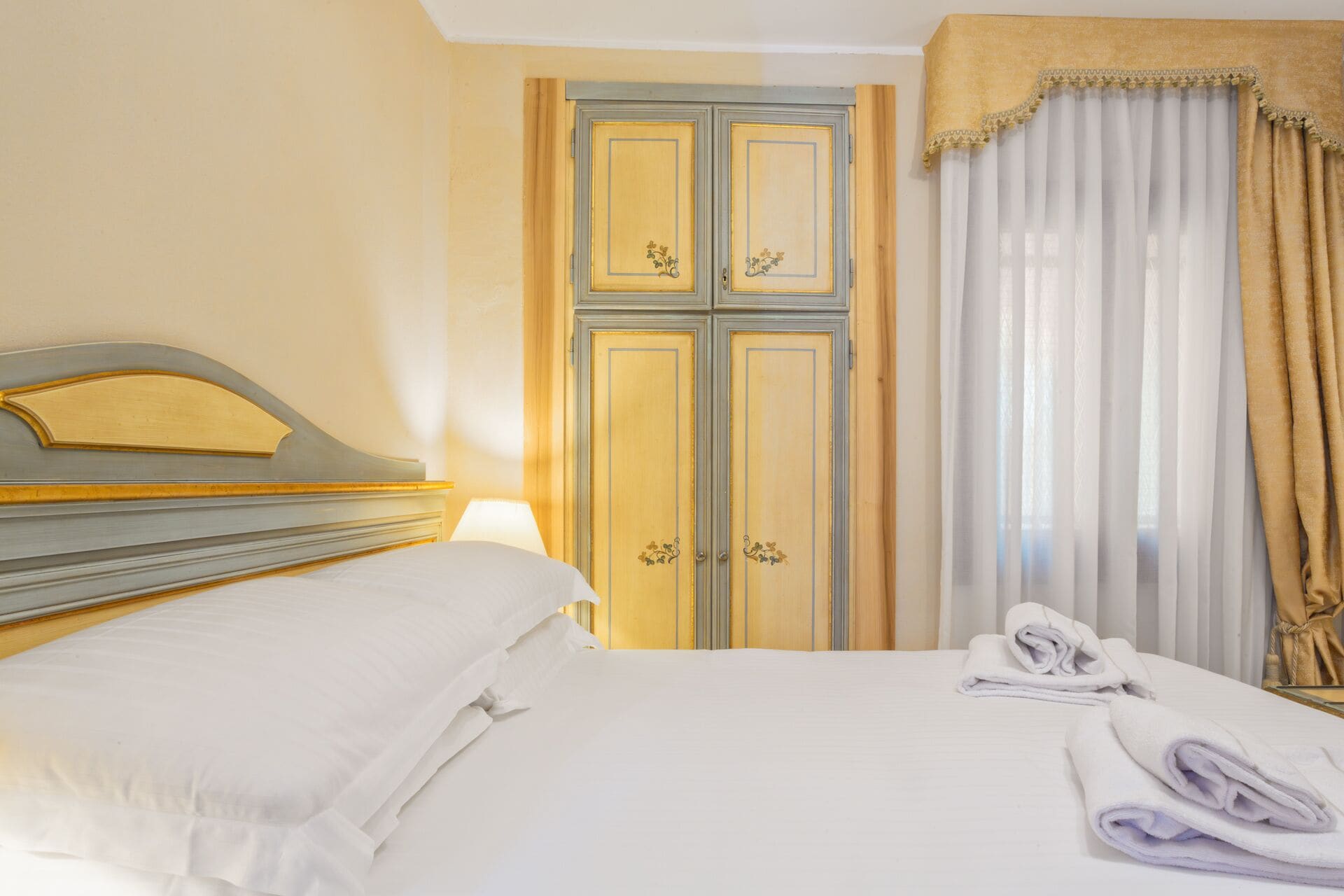 A hotel room with a bed, a wardrobe, and a window with curtains.