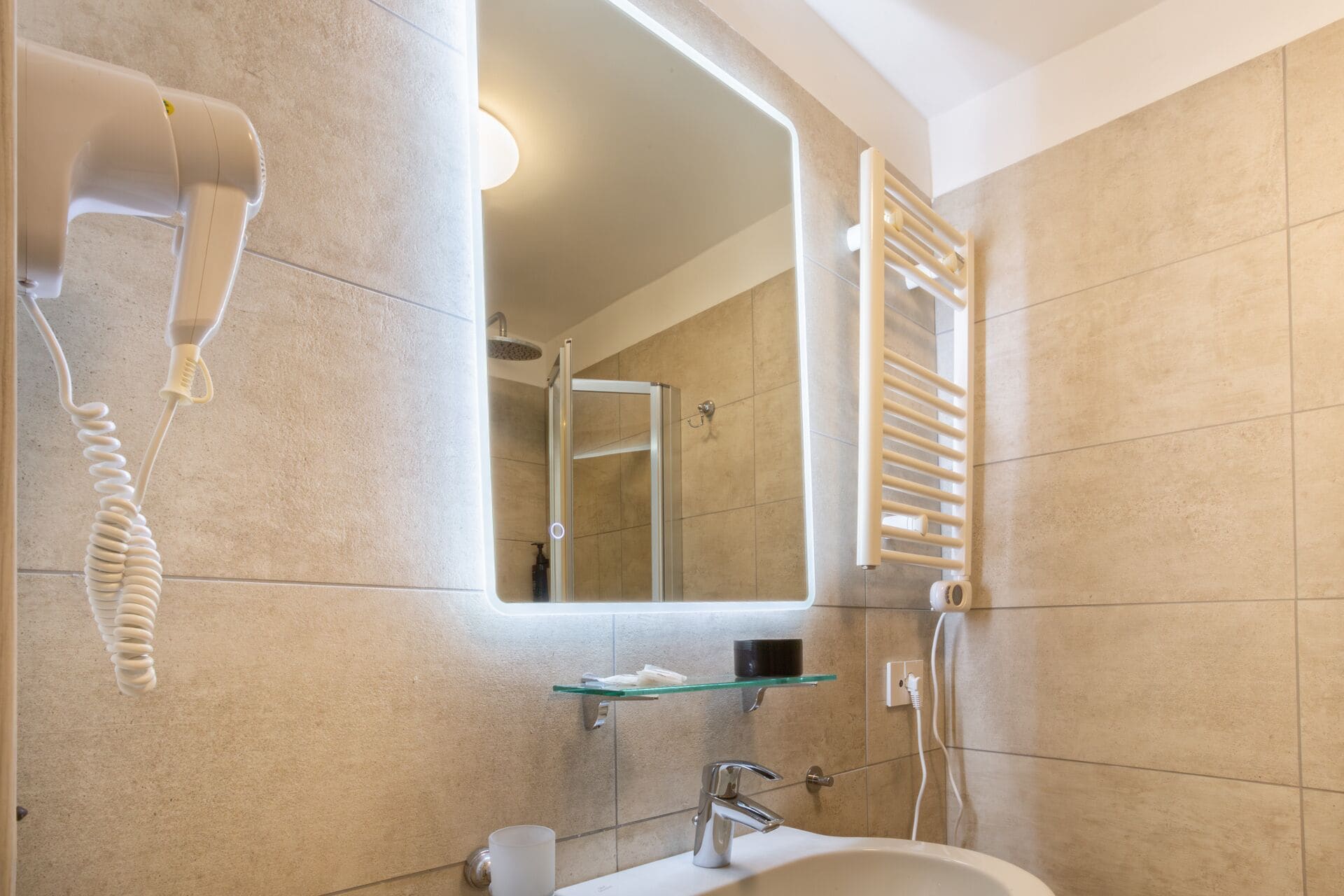 Une salle de bain avec une étagère en verre, un miroir, un sèche-cheveux et une douche.