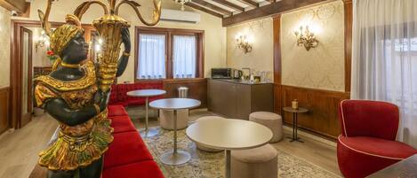 Une chambre d’hôtel avec un canapé rouge, une table à manger, un lustre et une statue décorative.