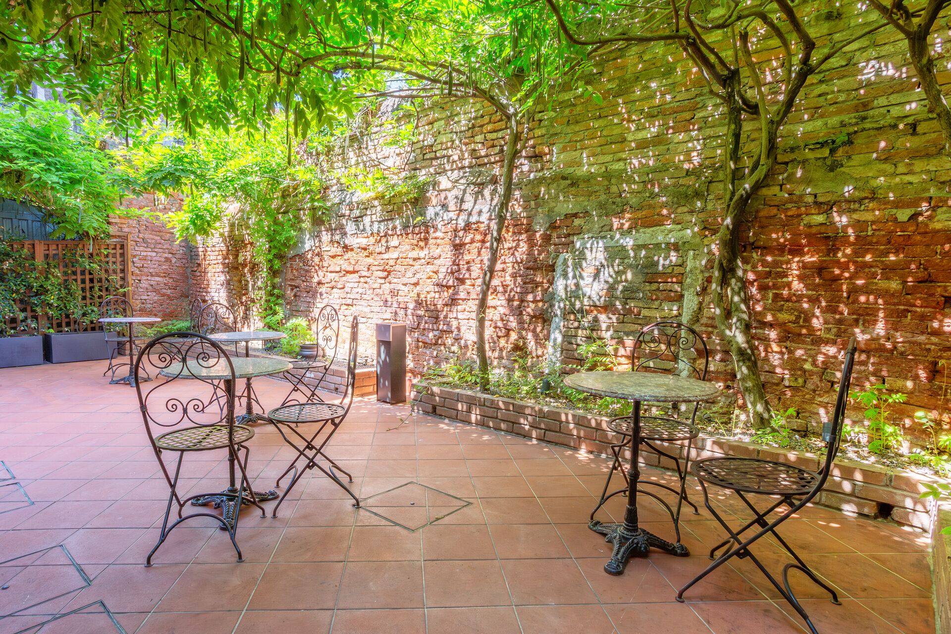 An outdoor patio with brick walls, metal tables and chairs, and greenery.