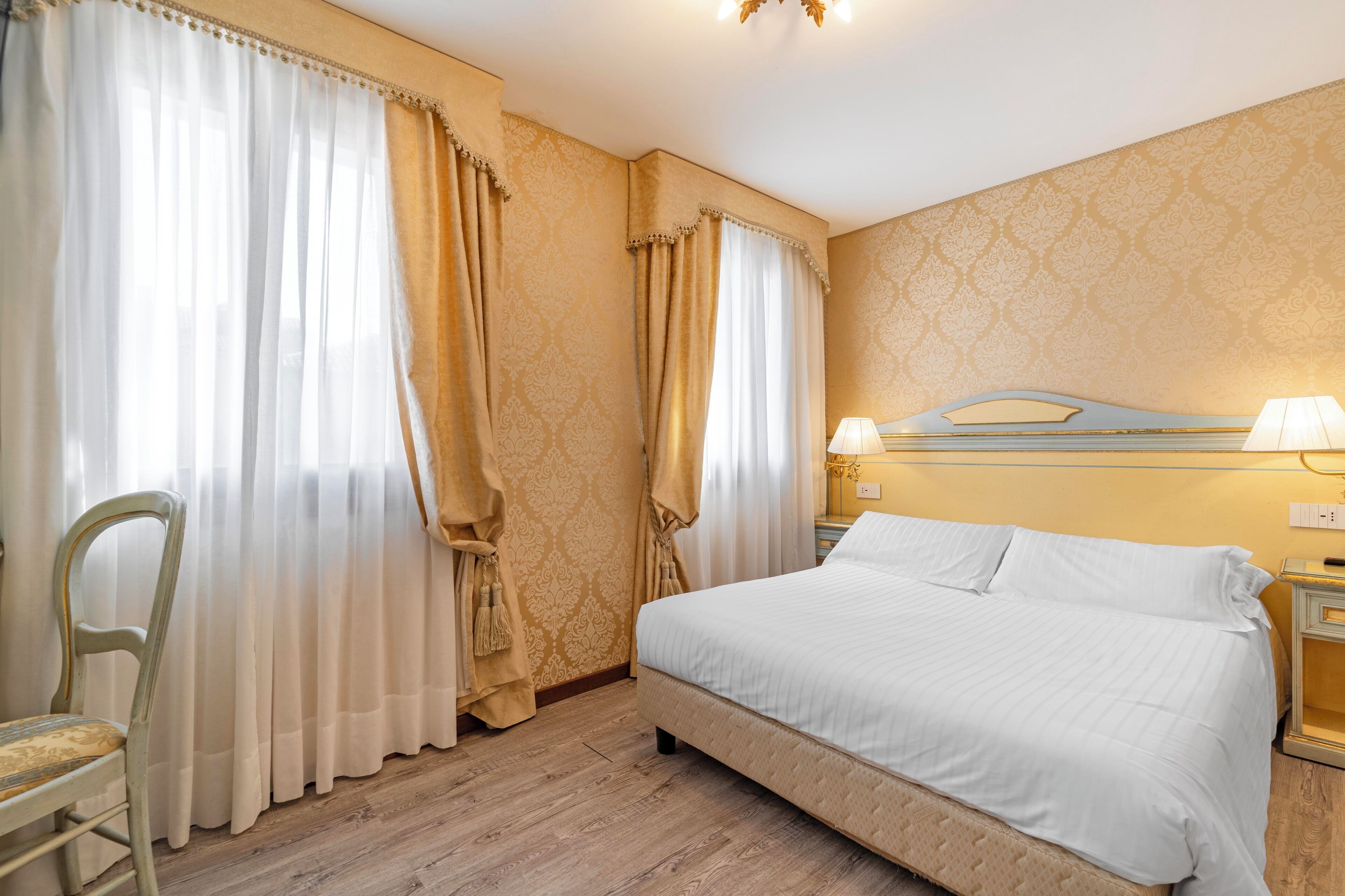 Habitación de hotel con cama, cortinas, una silla, mesita de noche y una pared con diseño decorativo.