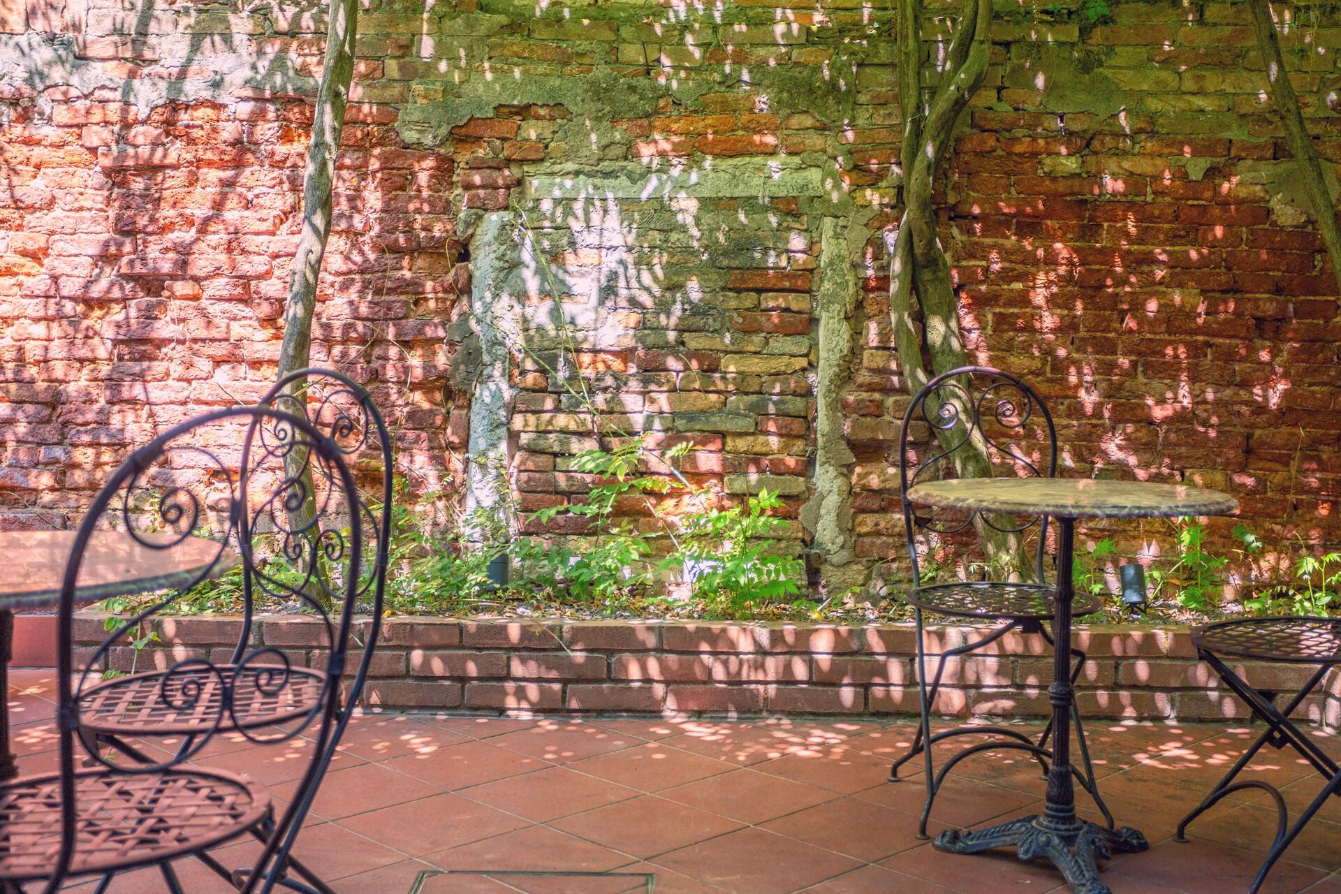 A brick wall with a metal table and two chairs in front.